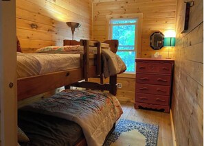 A cabin-style room with two bunk beds, a dresser, a window with a view, and a lamp. - Quiet cabin on Center Pond. (Lincoln)