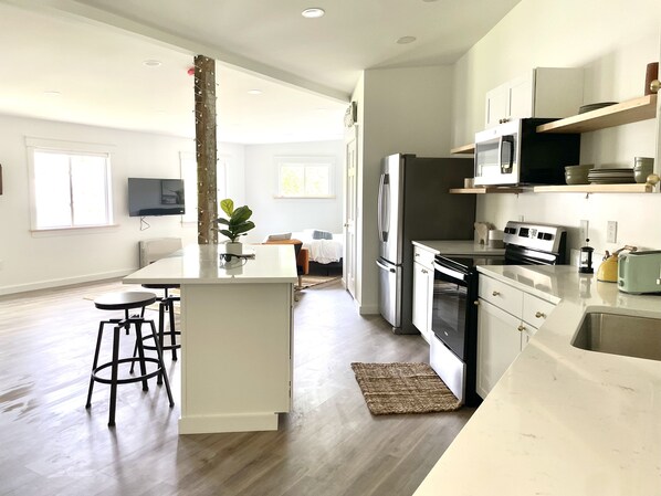 Una cocina moderna con una isla central, taburetes de bar, refrigerador, horno, microondas y un televisor montado en la pared.