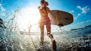 A person holding a surfboard at the beach with waves and the sun in the background. - Breathtaking Ocean View Condo (Jaco)