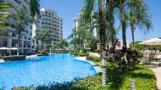 A swimming pool surrounded by palm trees and greenery, with adjacent multi-story buildings. - Breathtaking Ocean View Condo (Jaco)
