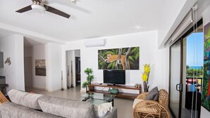 A modern living room with a sofa, a television, and a wicker chair. - Breathtaking Ocean View Condo (Jaco)