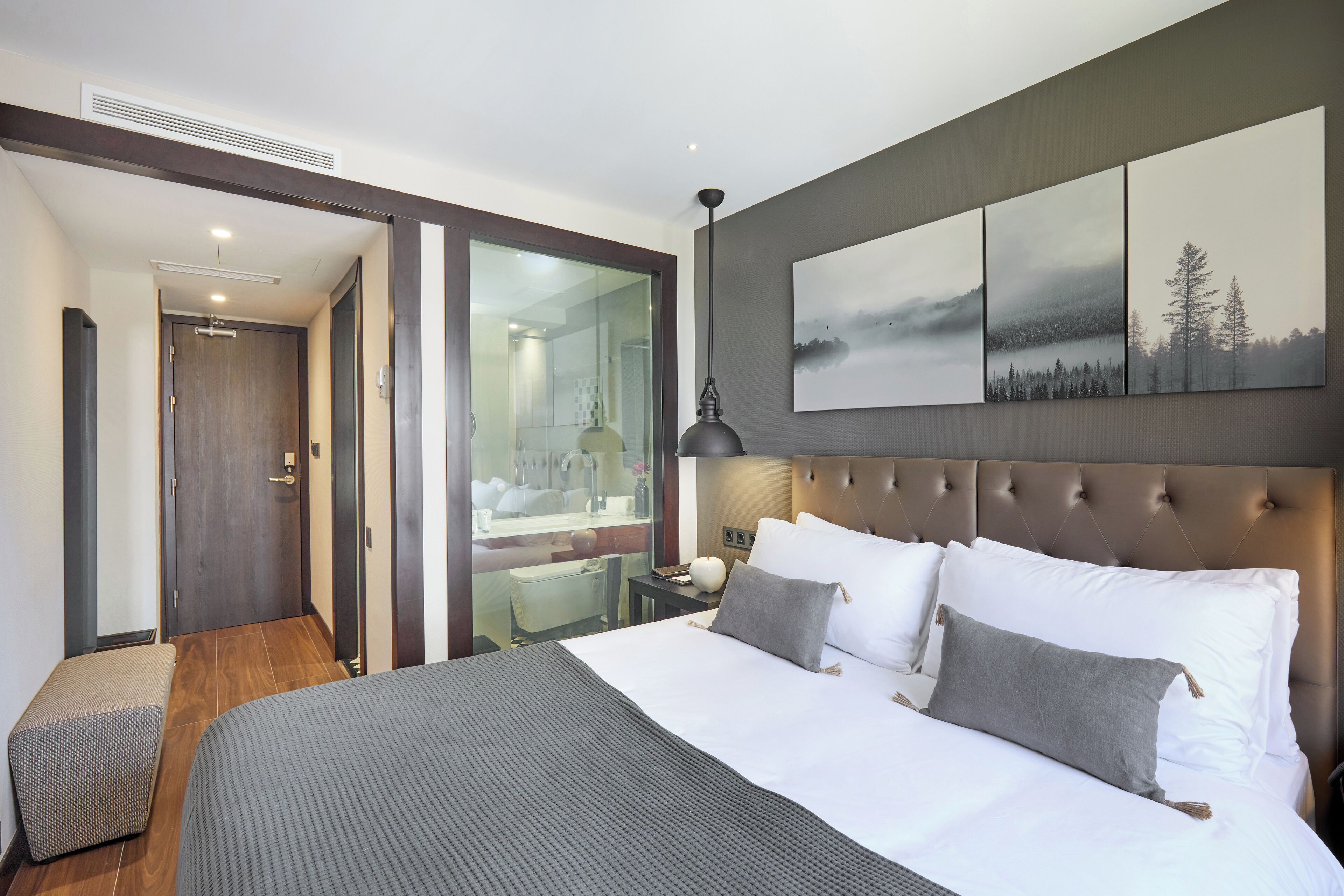 Ein modernes Hotelzimmer mit einem großen Bett, einem verglasten Badezimmer und Blick ins Freie.