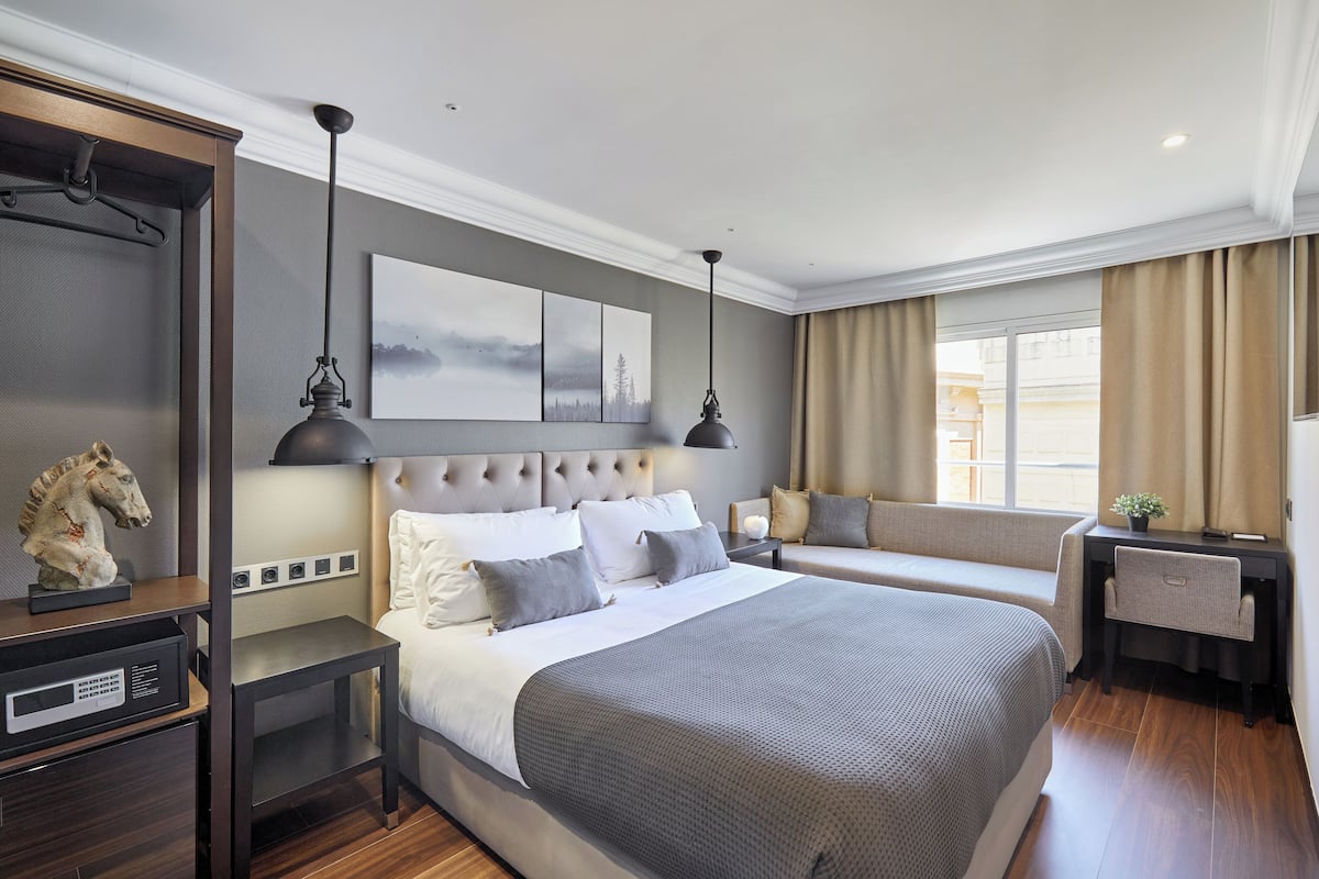 A modern hotel room with a large bed, a desk, and a seating area by the window.