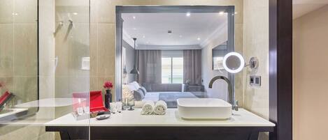 A modern bathroom with a glass-enclosed shower, a large mirror with a round light, and a white sink.