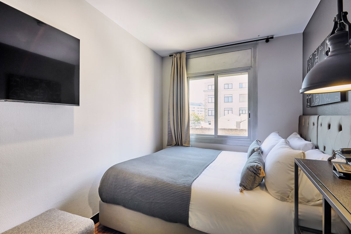 A modern hotel room with a large bed, a desk, and a window with curtains.