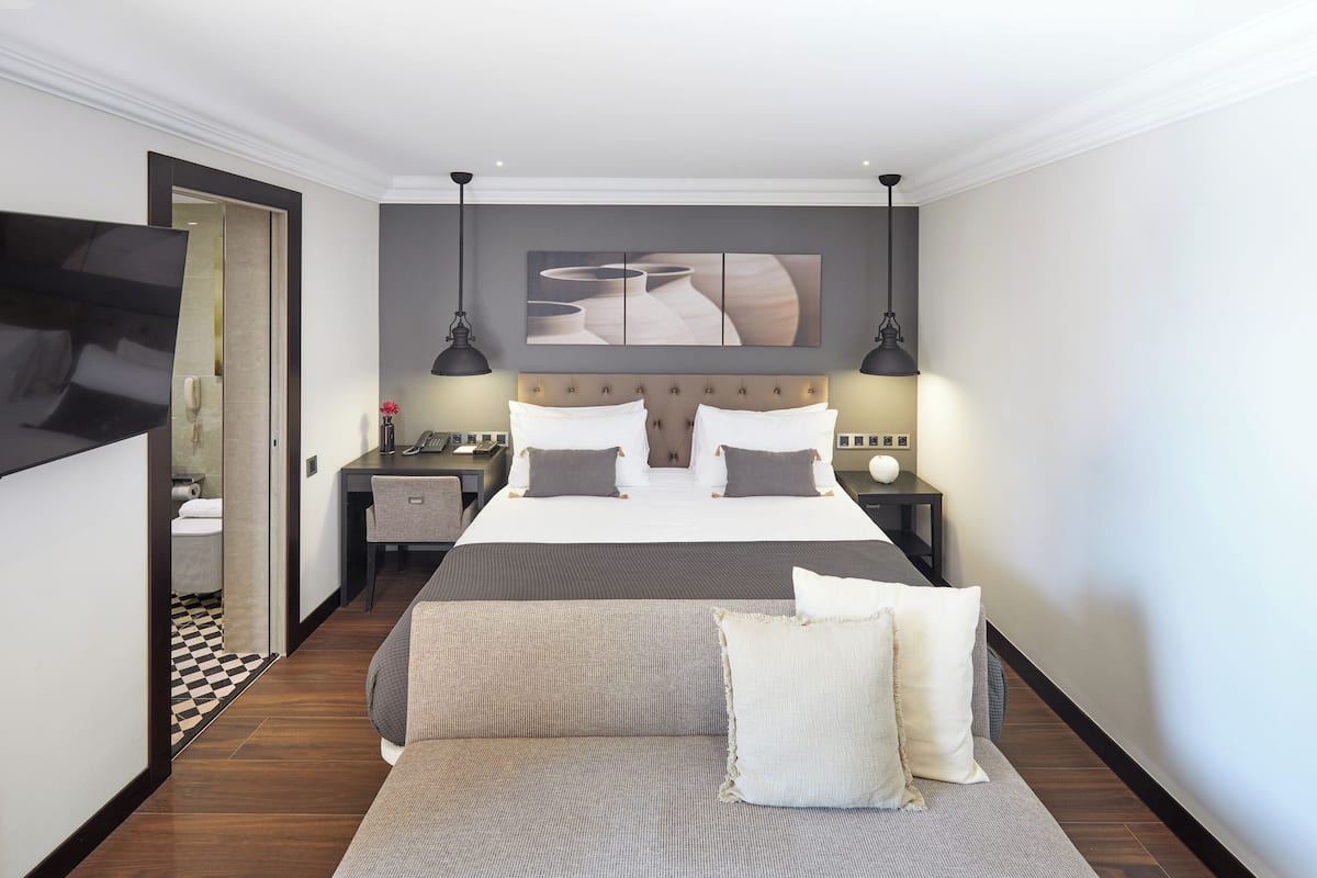 A modern hotel room with a large bed, a sofa, a flat-screen TV, and a painting on the wall.