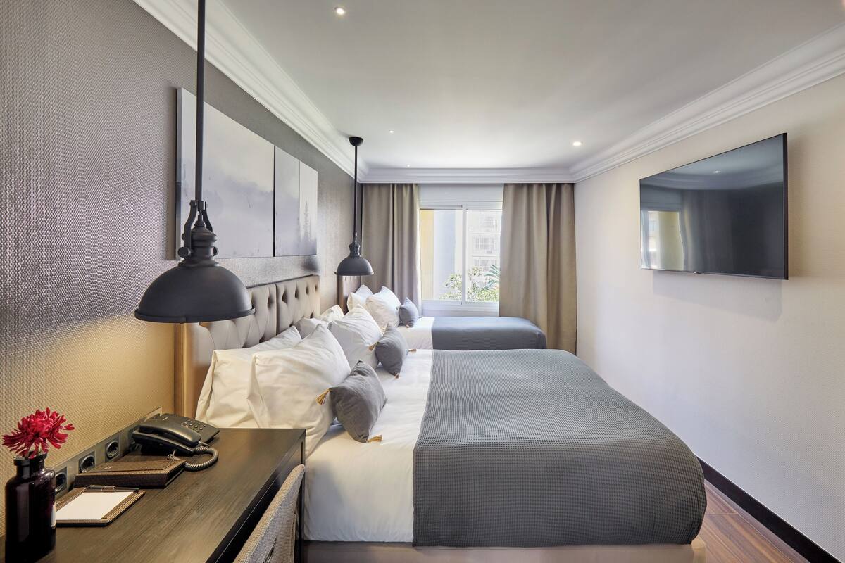 A hotel room with a large bed, bedside tables, a desk with a telephone, and a flat-screen TV mounted on the wall.
