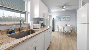 A modern kitchen with granite countertops, a sink, white cabinets, and a dining area with a table and chairs. - NEW BEACH LISTING, Walk-Beach, Surfing, Scuba, Close-Dining, Wi-Fi (West Palm Beach)