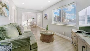 A modern living room with a green sofa, a round coffee table, and a view of the city through large windows. - NEW BEACH LISTING-Block To The Beach, Fishing Nearby, Surfing, Chairs (West Palm Beach)