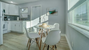 A modern kitchen with white cabinets, a dining area with white chairs, and a window with blinds. - NEW BEACH LISTING-Block To The Beach, Fishing Nearby, Surfing, Chairs (West Palm Beach)