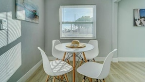 A room with a round table and four white chairs, a window with blinds, and two framed artworks on the walls. - NEW BEACH LISTING-Block To The Beach, Fishing Nearby, Surfing, Chairs (West Palm Beach)