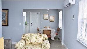 A living room with a floral sofa, a dining area with a table and chairs, and a hallway leading to another room. - NEW BEACH LISTING -Walk To Beach, BBQ Grill, Scuba, Beach Chairs (West Palm Beach)