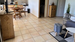 A modern living room with a wooden dining table, chairs, a TV on a wooden stand, a clock on the wall, and a small cabinet. - Le nid Capcinois (Formiguères)