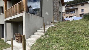 A modern two-story house with a balcony, a stone staircase, and a grassy hill. - Le nid Capcinois (Formiguères)