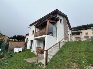 A two-story house with a balcony, a stone wall, and a wooden staircase leading to the entrance. - Le nid Capcinois (Formiguères)