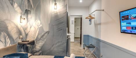 Une chambre d’hôtel moderne avec un grand lit, un téléviseur fixé au mur et un papier peint à motifs tropicaux.