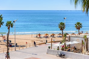 A beachside promenade with palm trees, beach umbrellas, and a sea view.