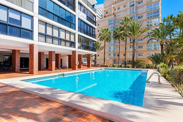 A hotel with a swimming pool, outdoor seating, and palm trees.