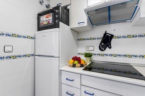 Cozinha equipada com geladeira, micro-ondas e fogão. Os armários têm puxadores azuis e há uma cesta de frutas no balcão.