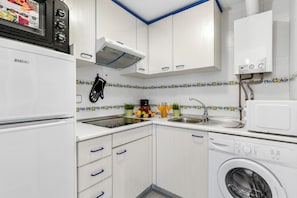 A compact kitchen with white cabinets, a built-in oven, a microwave, a sink, and a washing machine.