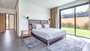 Un dormitorio moderno con una cama grande, una mesita de noche pequeña y vistas a un jardín a través de un ventanal corredero.