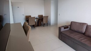 A modern living room with a sofa, a dining table with chairs, and a large mirror. - Ap Praia de Ouro - Venice Home Club (Picarras)