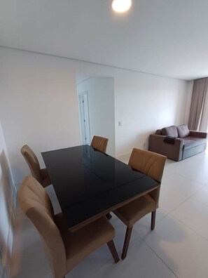 A modern living room with a dining table and chairs, a sofa, and a door leading to another room. - Ap Praia de Ouro - Venice Home Club (Picarras)