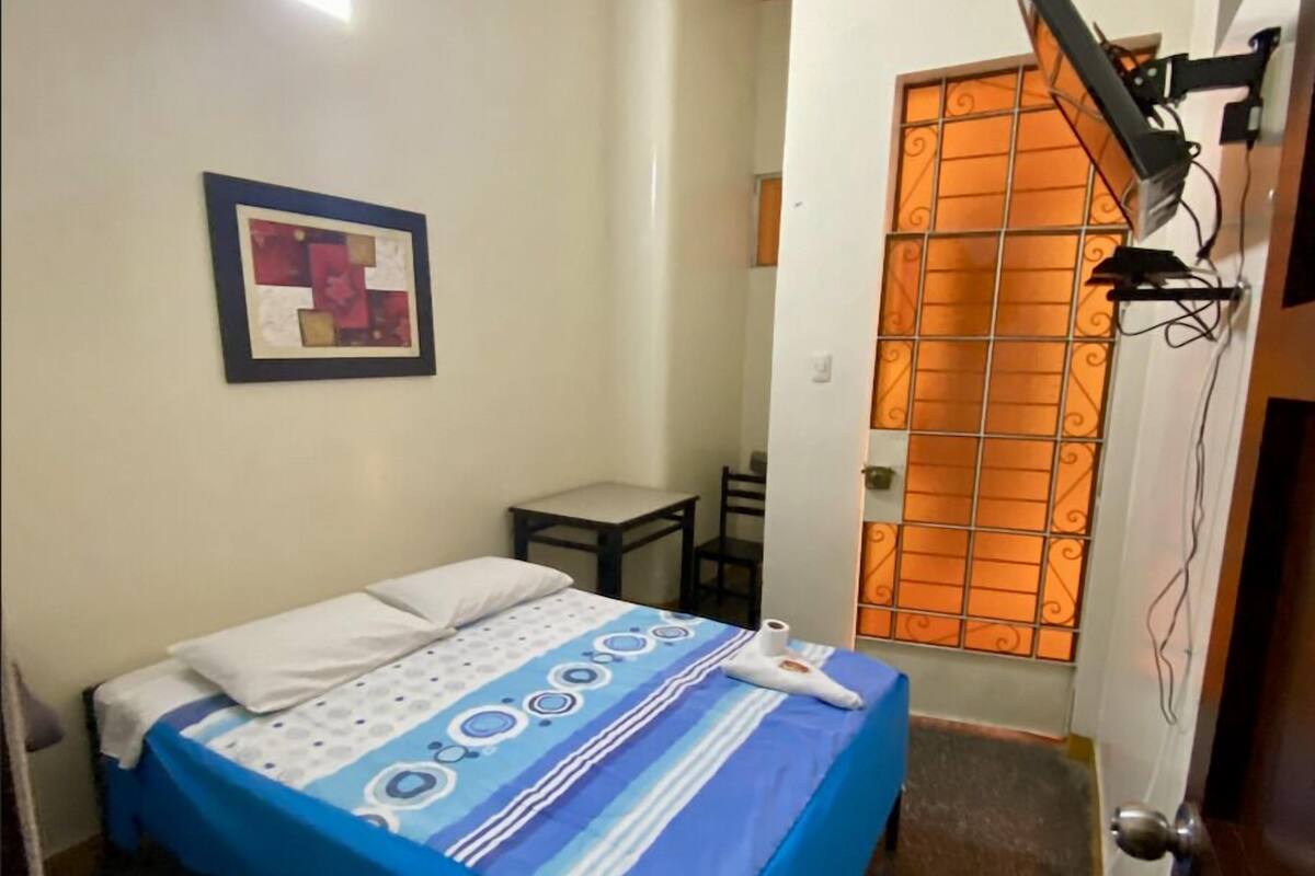A small, neatly arranged room with a bed, a desk, and a chair.