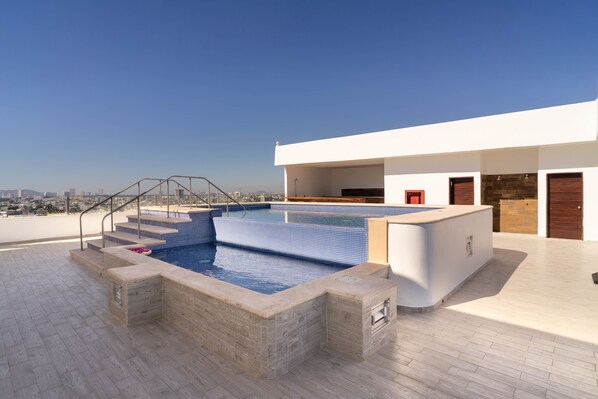 A rooftop pool with a clear view of the city skyline, a modern architectural design, and a spacious deck area.