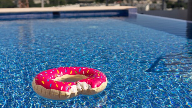 Une piscine avec une eau d’un bleu limpide et un flotteur rose en forme de beignet.