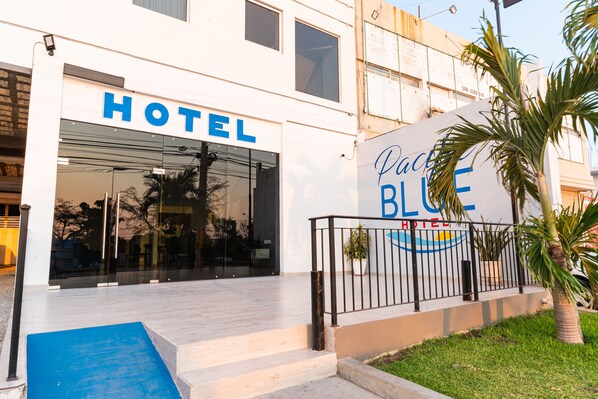Entrada de un hotel con fachada de vidrio, una rampa azul y un letrero que dice 'Hotel Blue'.