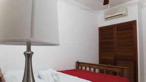 Een hotelkamer met een bed, een houten hoofdbord, een rood-wit gebeddeken, een wit kussen en een plafondventilator.