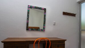 Een houten bureau met een stoel, een spiegel met een bloemenversiering en een kapstok.