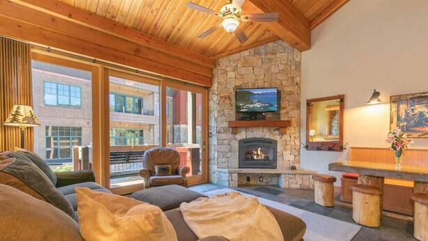A cozy living room with a stone fireplace, comfortable seating, and a television mounted above it. - Ski-in/Ski-out Northstar Condo (Truckee)