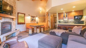 A cozy living room with a stone fireplace, a television, and a dining area with stools. - Ski-in/Ski-out Northstar Condo (Truckee)