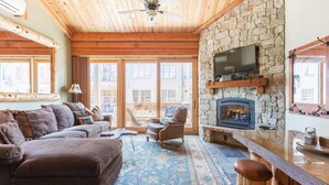 A cozy living room with a stone fireplace, a television mounted on the wall, and a wooden ceiling. - Ski-in/Ski-out Northstar Condo (Truckee)