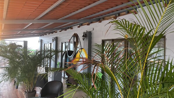 Un espace extérieur abrité, aménagé avec des sièges, des plantes en pot et une structure métallique au plafond.