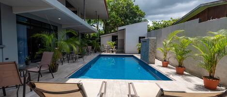 A modern outdoor pool area with lounge chairs, potted plants, and a clear blue pool.