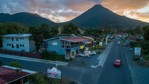 Straßenansicht mit einem Berg im Hintergrund, einem blauen Gebäude mit der Aufschrift 'MINI MARKET' und einem roten Auto auf der Straße.