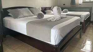 Ein Hotelzimmer mit zwei Betten, einem großen Fenster mit Vorhängen, einer Wandklimaanlage und einem Bild an der Wand.