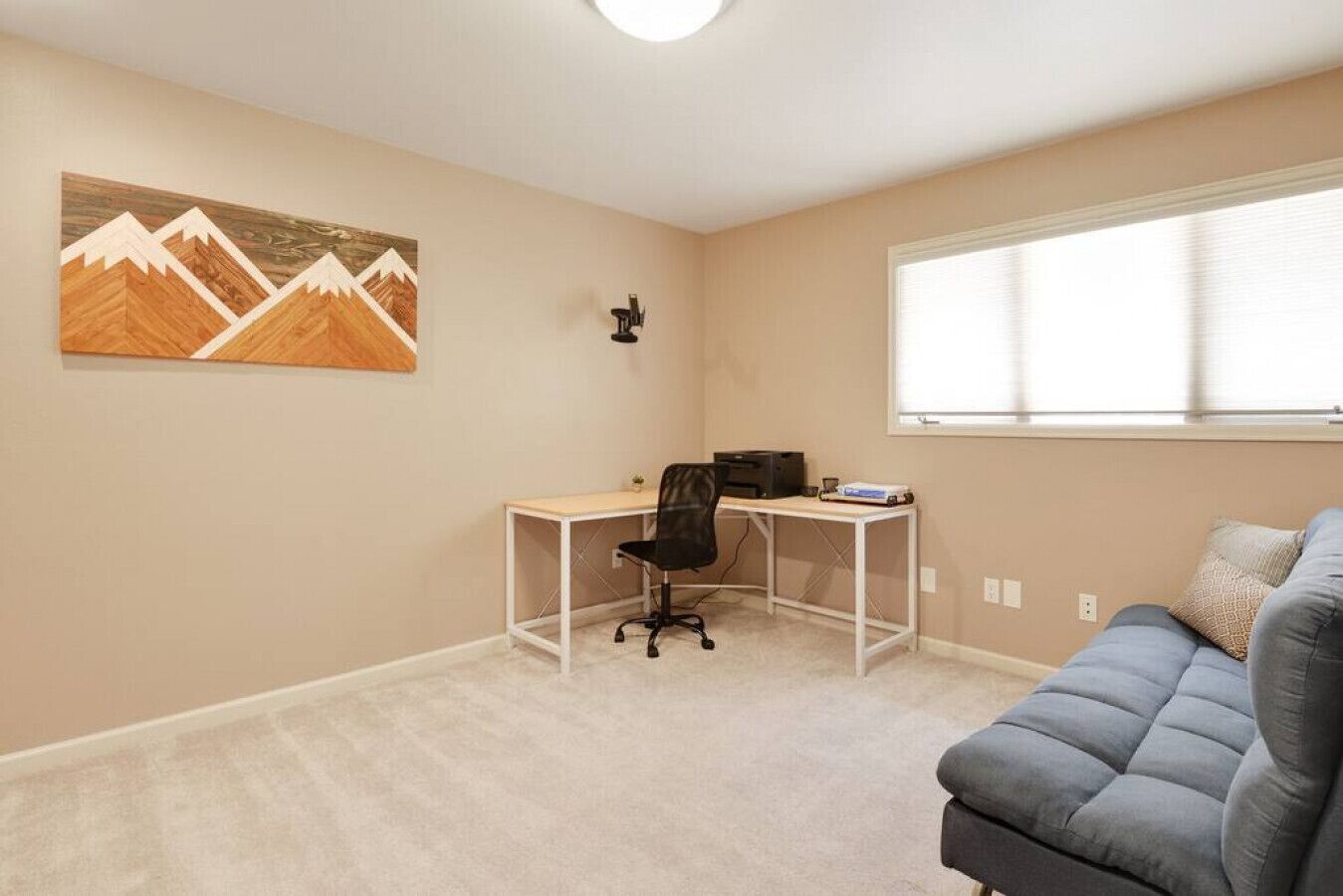 Quarto com escrivaninha, cadeira e sofá cinzento.