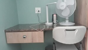 A workspace with a desk, chair, and a standing fan.