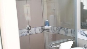 A modern bathroom with a glass shower enclosure, a marble-tiled vanity, and a white sink.