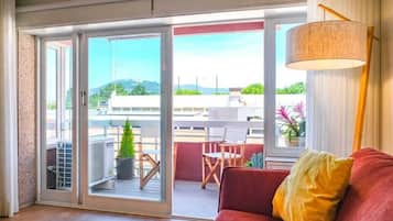 A room with a red sofa, a yellow pillow, a large window, and a view of the outdoors.