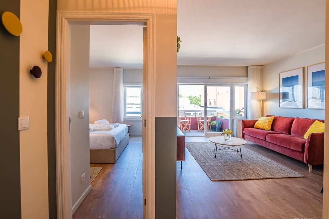 Une chambre d’hôtel moderne avec un lit, un canapé rouge, une table basse et une vue sur l’extérieur.