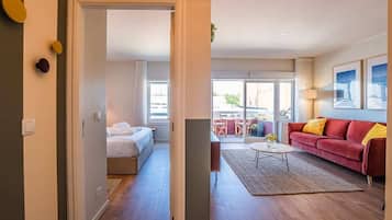Une chambre d’hôtel moderne avec un lit, un canapé rouge, une table basse et une vue sur l’extérieur.