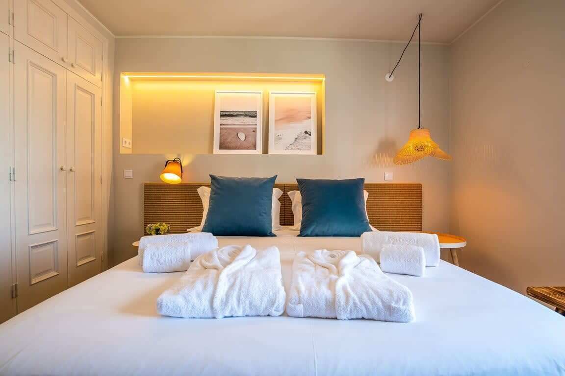 A hotel room with a large bed, two pillows, a bedside table, a lamp, and a wall-mounted picture.