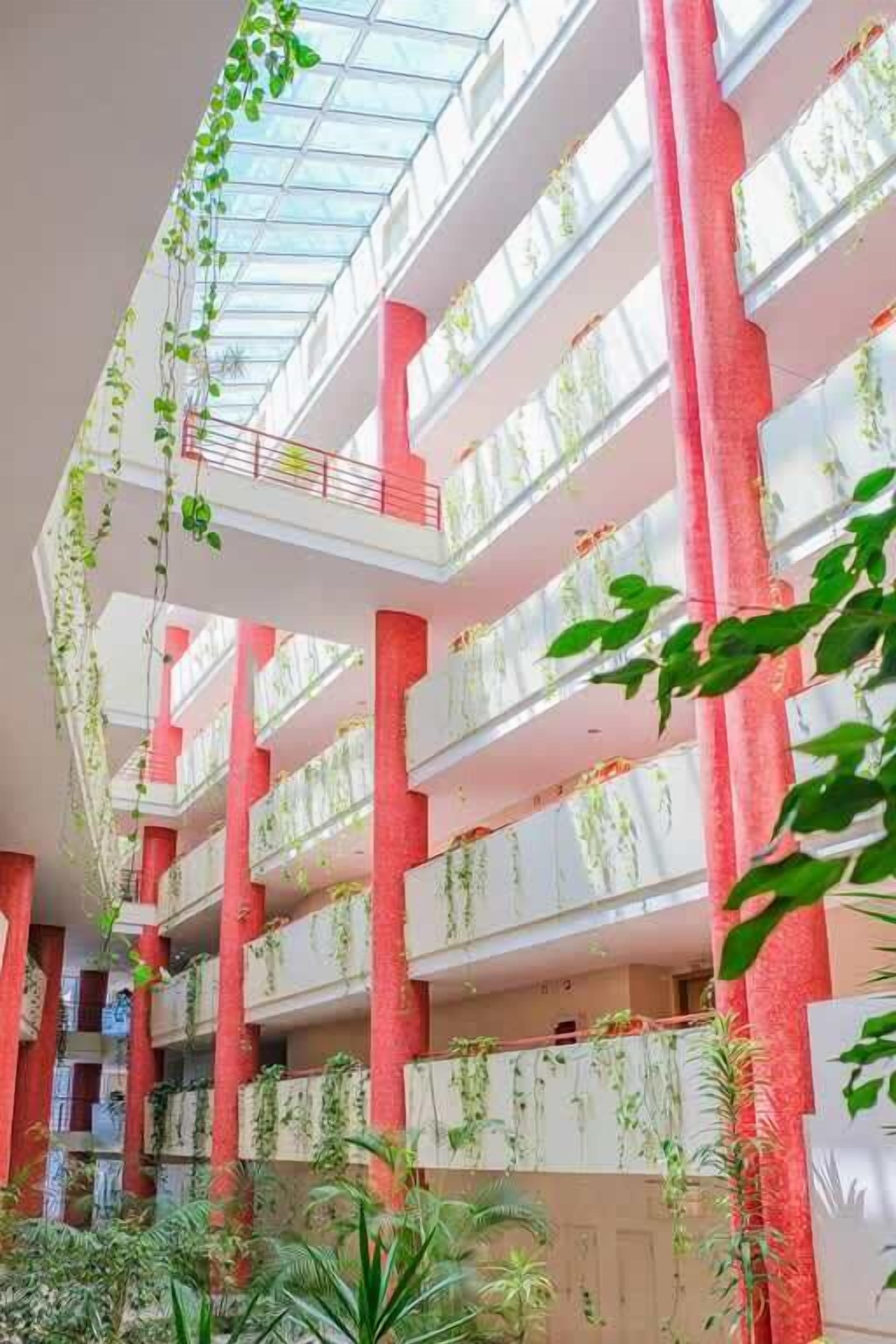 A multi-level atrium with hanging plants, red pillars, and a glass ceiling.