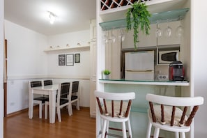 A dining area with a white table and chairs, a glass-top bar counter with a hanging plant, and a microwave above it. - (1008) Apartamento com 1 Quarto e Vista para o Cristo (Rio de Janeiro)