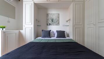 Quarto com uma cama, mesa de cabeceira, luminária na parede e um quadro.